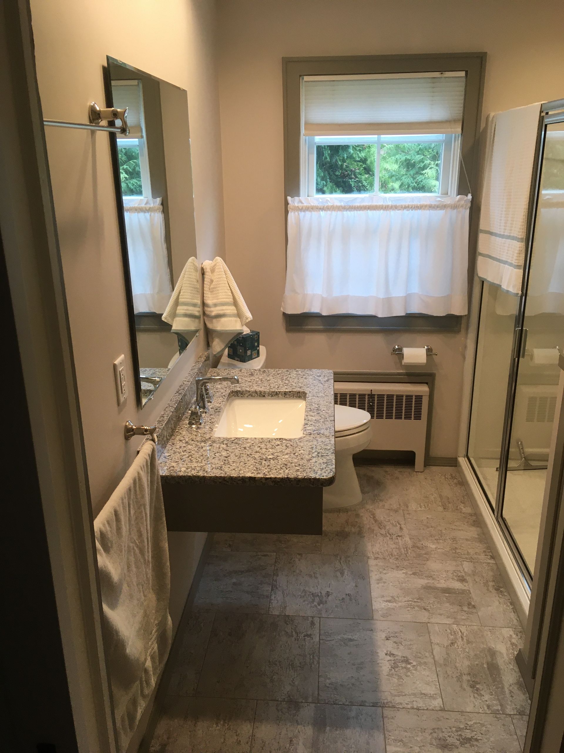 A bathroom with a sink , toilet , mirror and window.