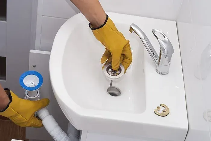 A person wearing yellow gloves is cleaning a bathroom sink.