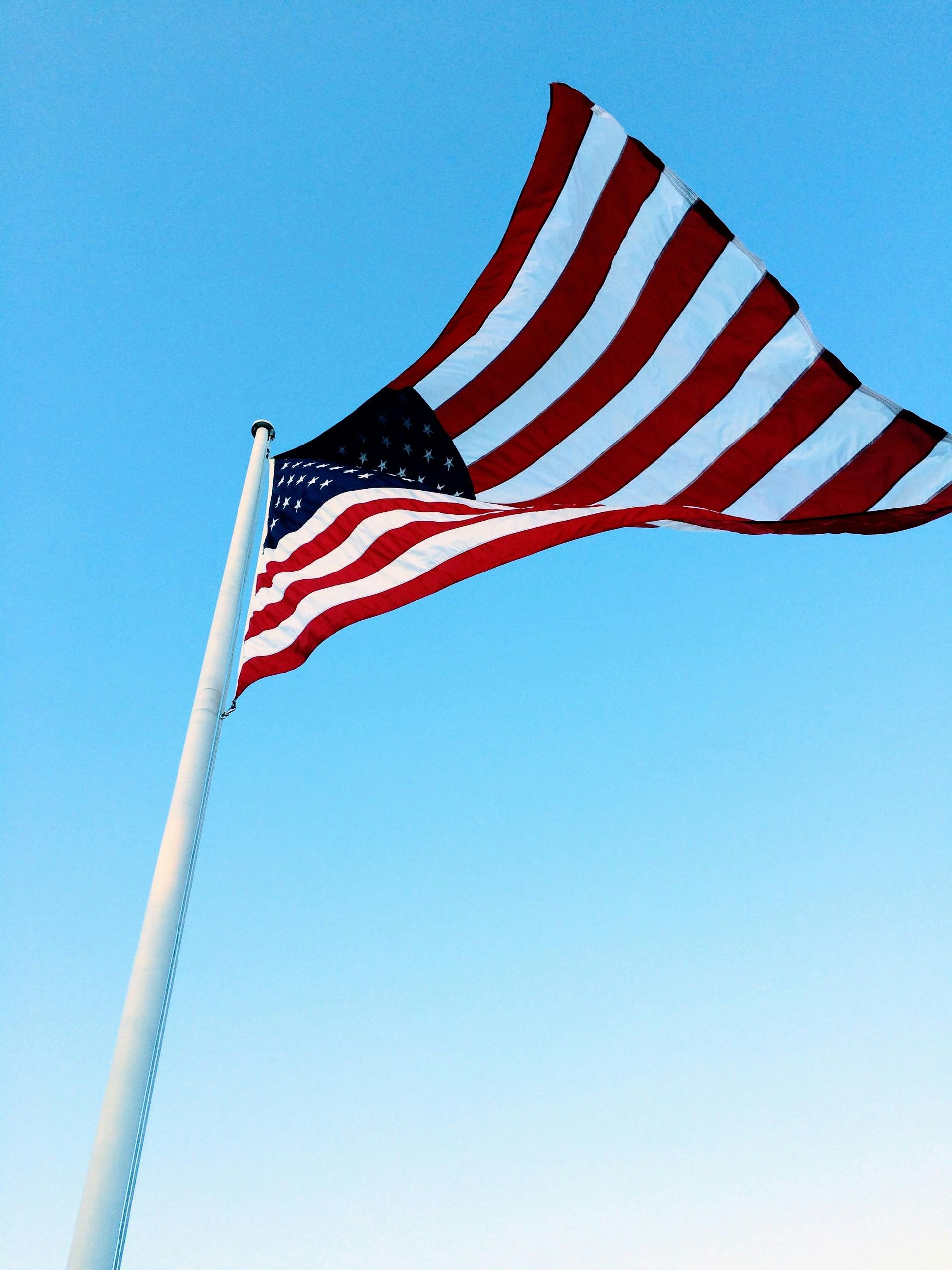 An american flag is flying in the wind against a blue sky