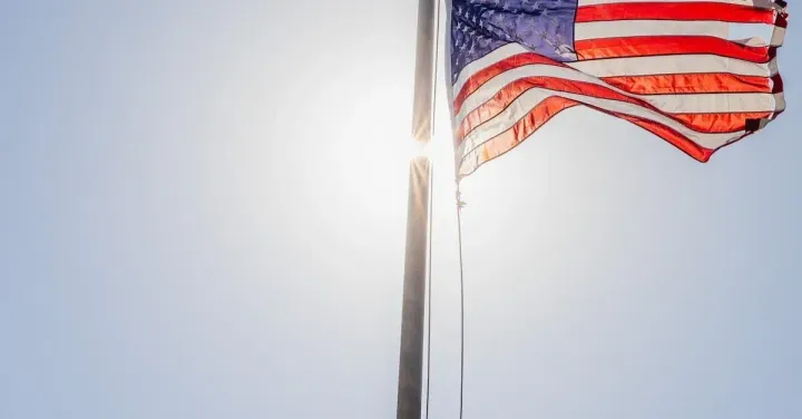 A large american flag is flying in the wind against a blue sky.