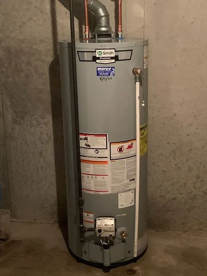 A water heater is sitting in a basement next to a wall.