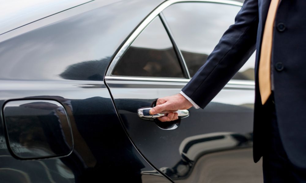 A man in a suit and tie is opening the door of a car.