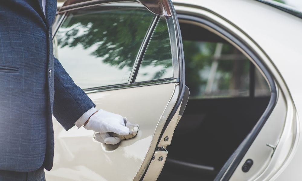 A man in a suit and white gloves is opening the door of a car.