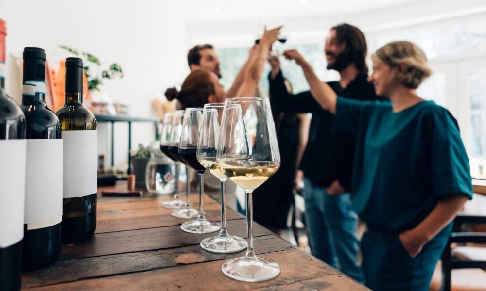 A group of people are standing around a table with bottles of wine and wine glasses.