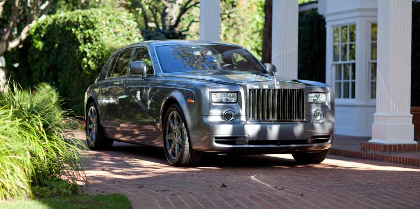 A gray rolls royce phantom is parked in front of a house.