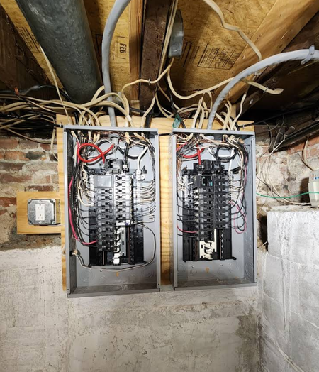 Two electrical panels are hanging from the ceiling in a basement
