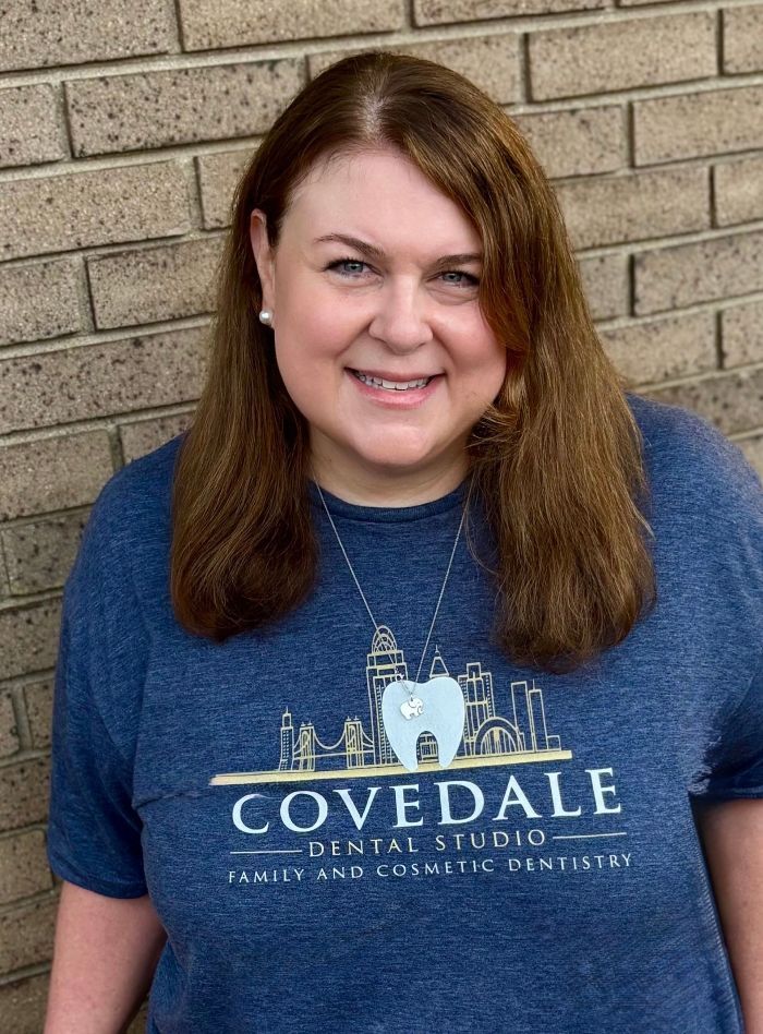 A woman wearing a blue t-shirt with a tooth on it is standing in front of a brick wall.