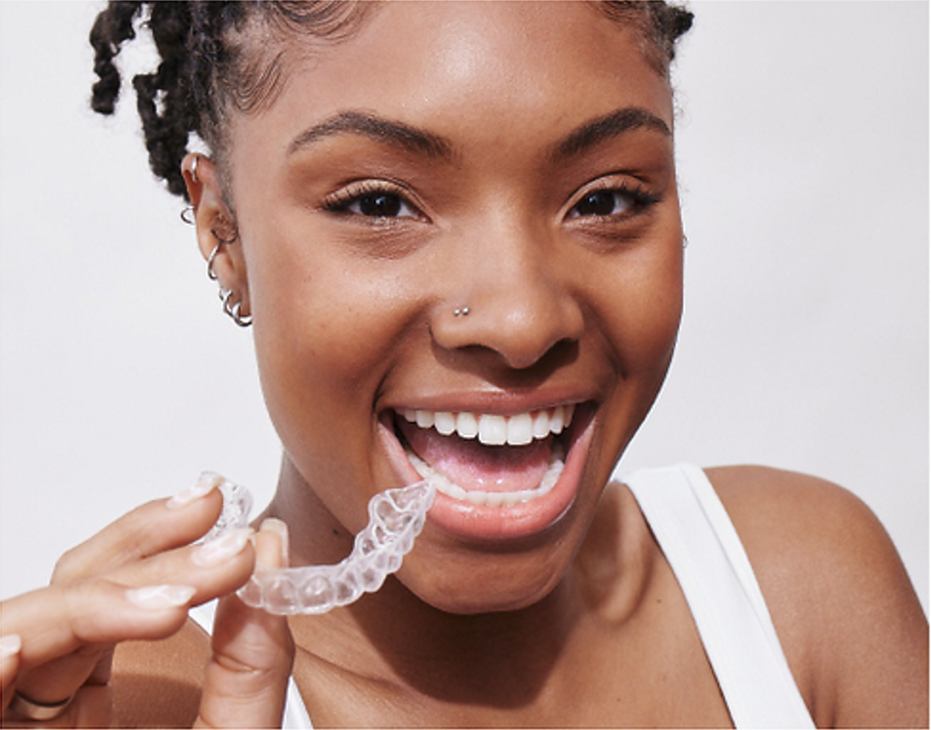 A woman is smiling while holding a clear brace in her mouth.