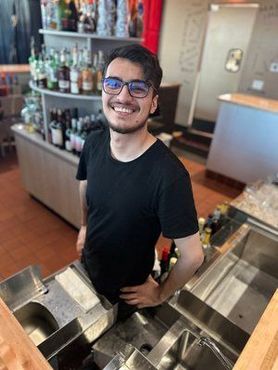 A man wearing glasses is standing behind a counter in a restaurant.