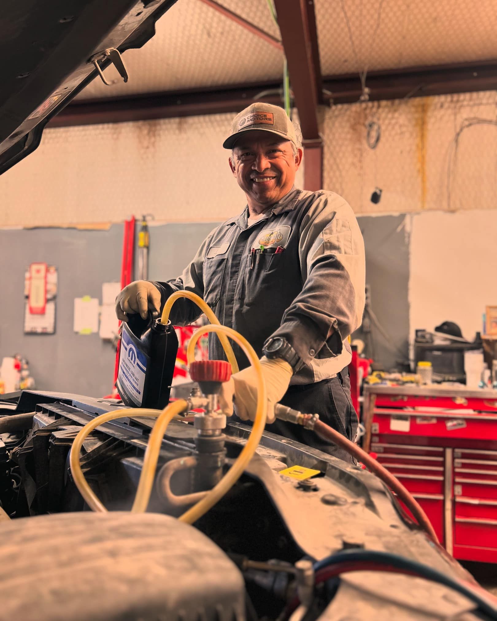 Mechanic smiles while filling car radiator with fluid in a garage.
