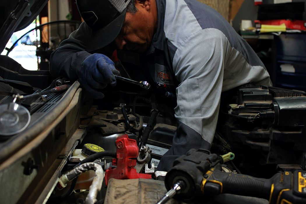 Mechanic working on car engine, using tools in an indoor garage setting.