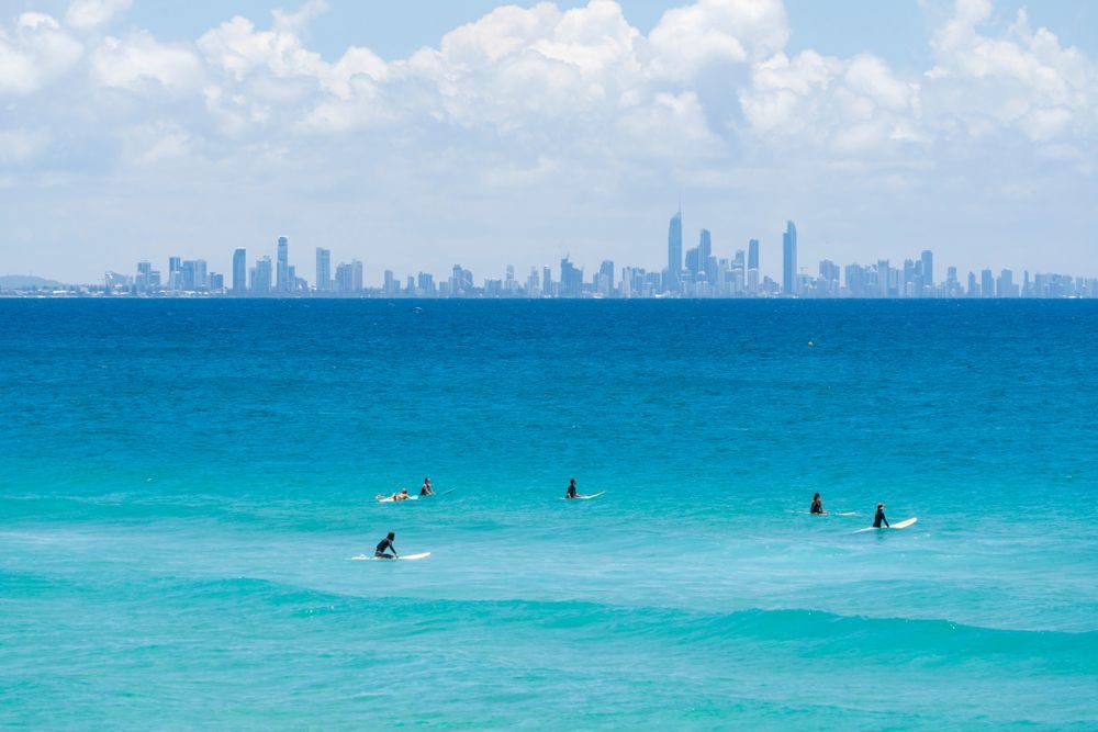 A Group Of People Are Surfing In The Ocean With A City Skyline In The Background — Australian Rock Walls In Gold Coast, QLD