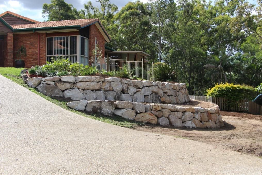 A Brick House With A Stone Wall In Front Of It — Australian Rock Walls In Bundaberg, QLD