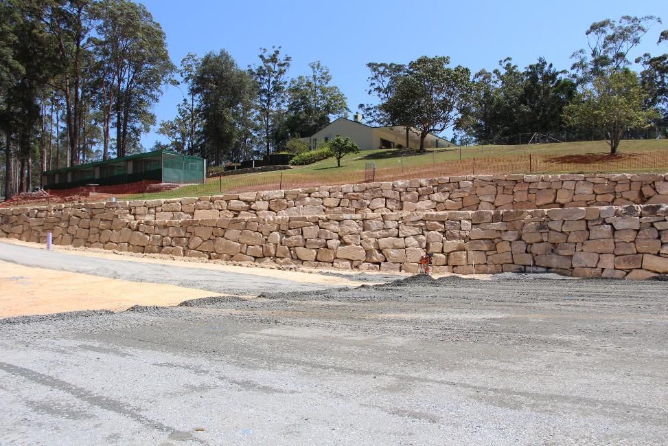 A Large Stone Wall Is Surrounded By Gravel And Trees — Australian Rock Walls In Burleigh Heads, QLD
