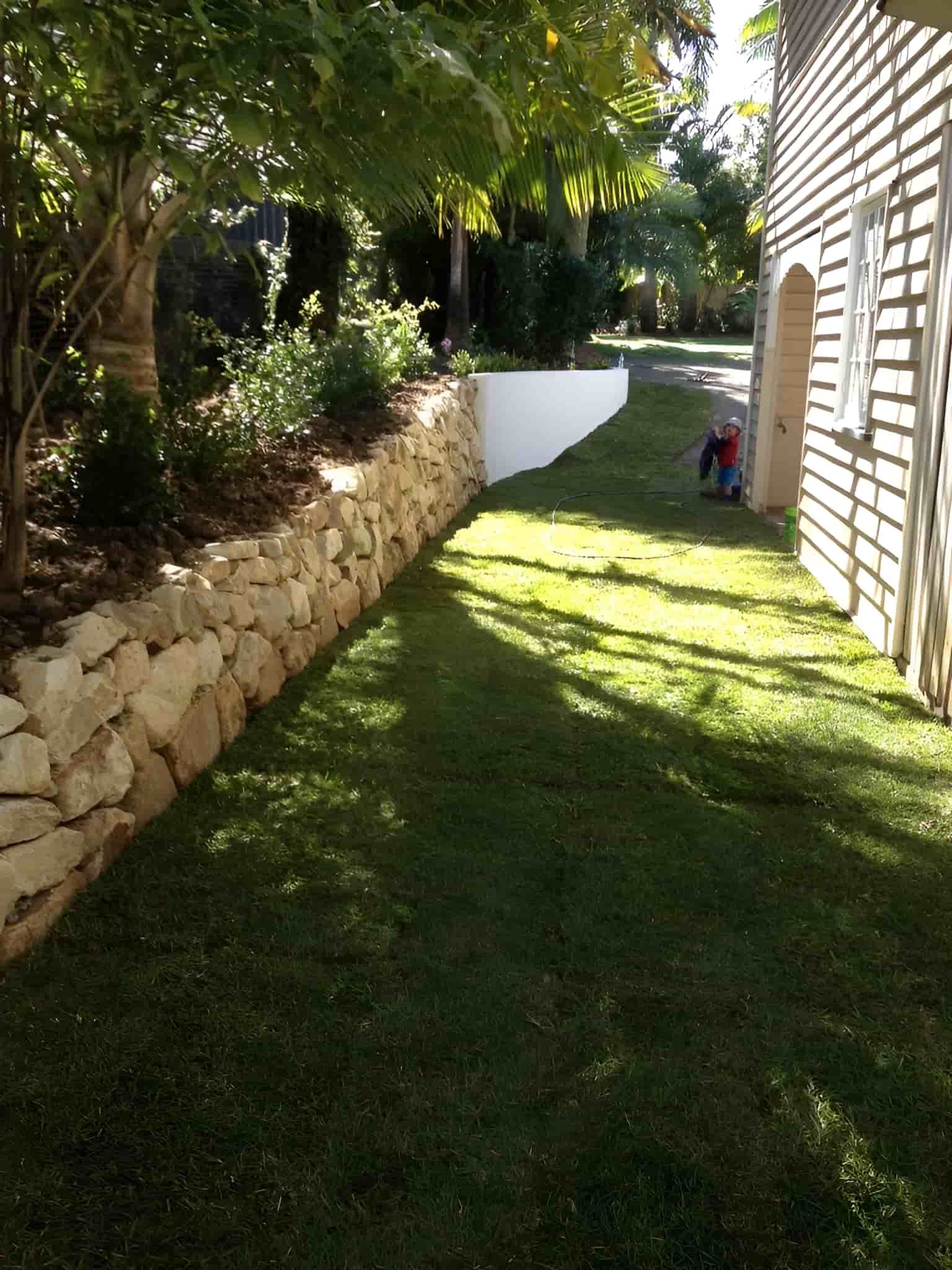 A Stone Wall Surrounds A Lush Green Lawn In Front Of A House — Australian Rock Walls In Burleigh Heads, QLD