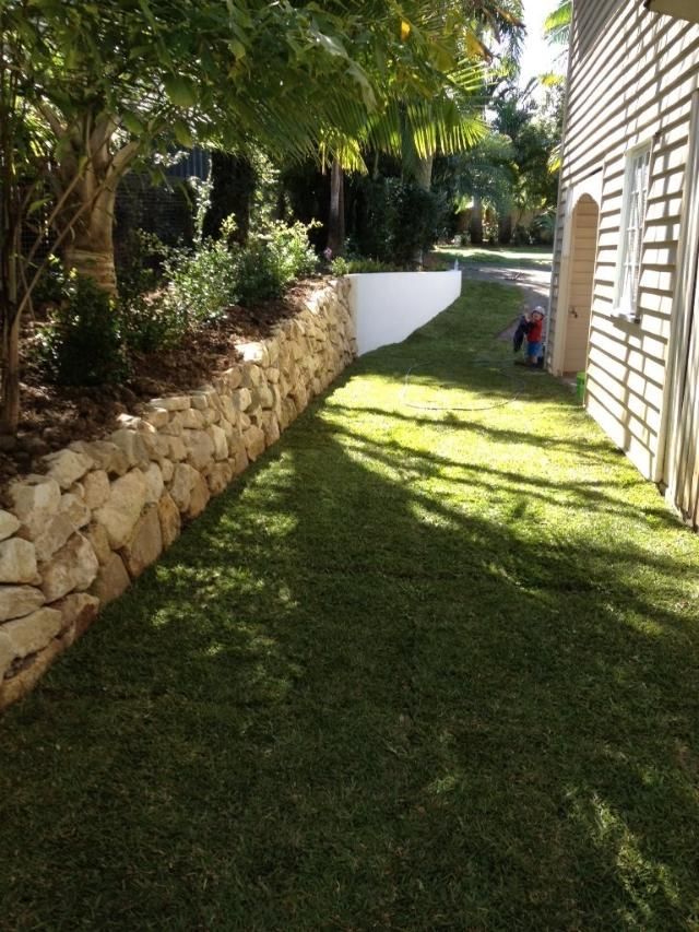 A Person Is Kneeling In The Grass Next To A Stone Wall — Australian Rock Walls In Burleigh Heads, QLD