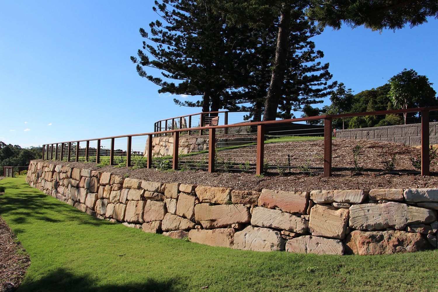 Stone Retaining Wall With A Wooden Railing And Green Grass