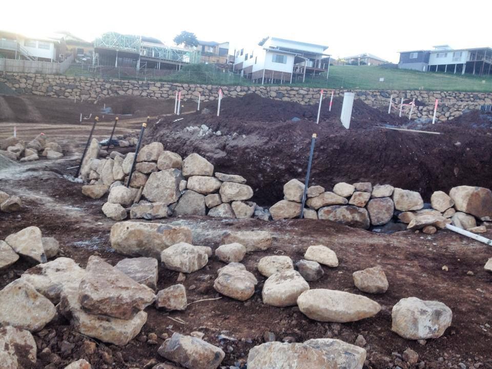 A Pile Of Rocks In A Dirt Field With A House In The Background — Australian Rock Walls In Upper Coomera, QLD