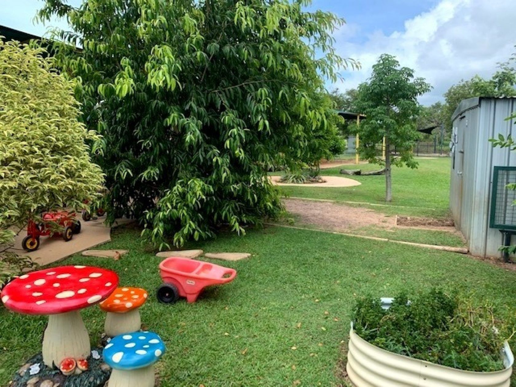 Playground with mushroom seats, a wheelbarrow, and a green grassy area.