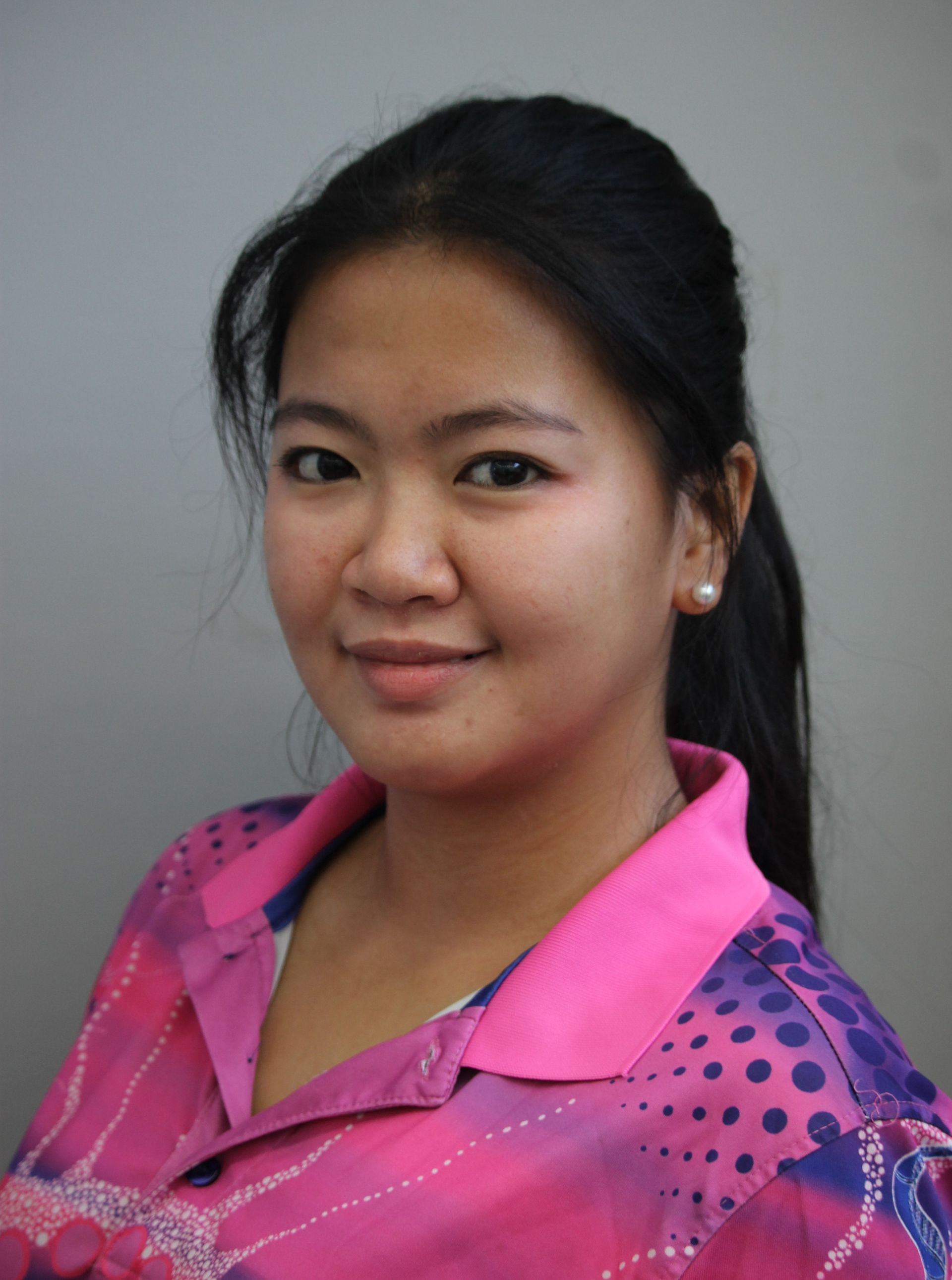 Young woman in pink shirt with dark hair, looking at the camera, smiling.