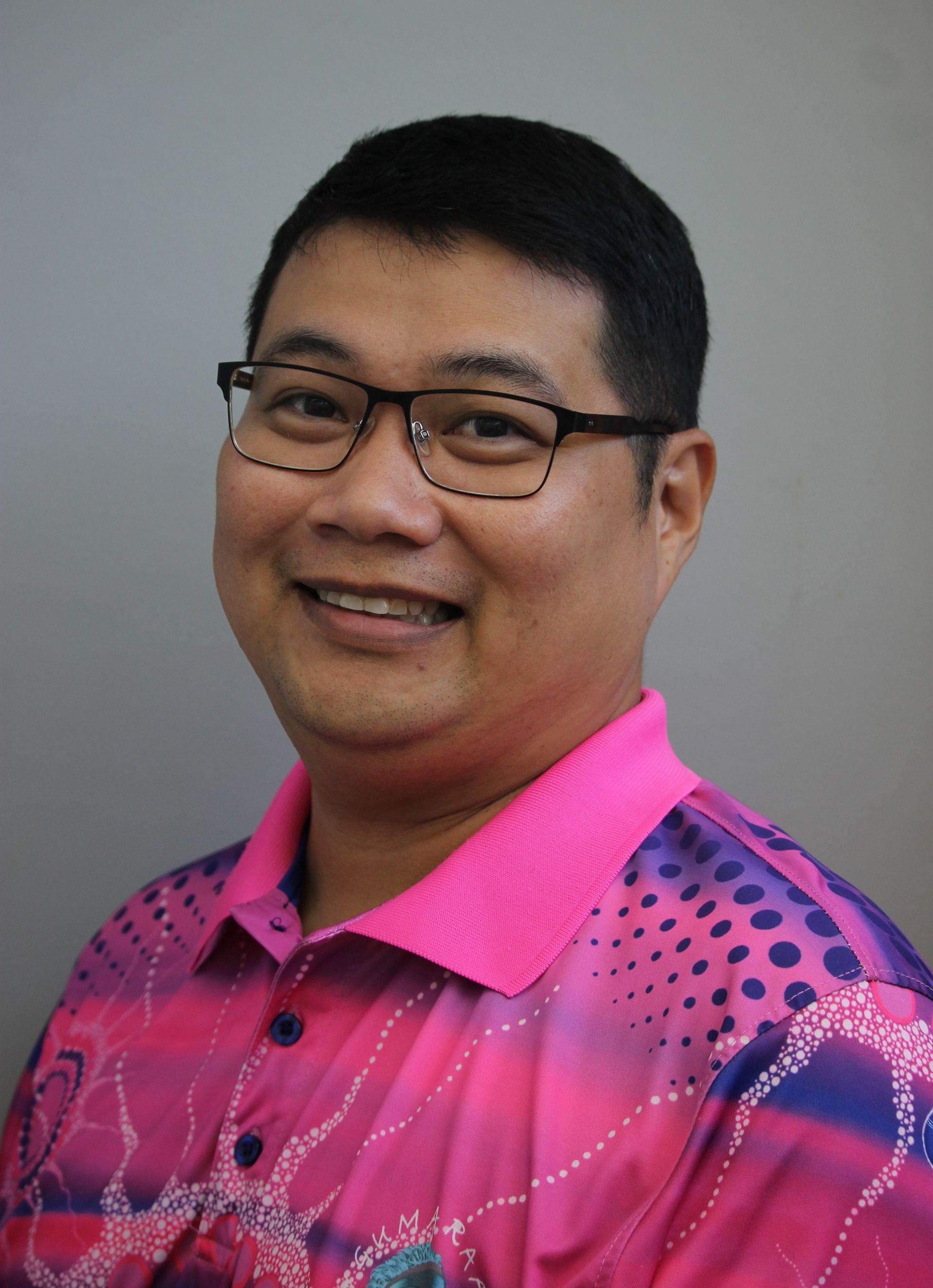 Man with glasses, wearing pink patterned shirt, smiling.