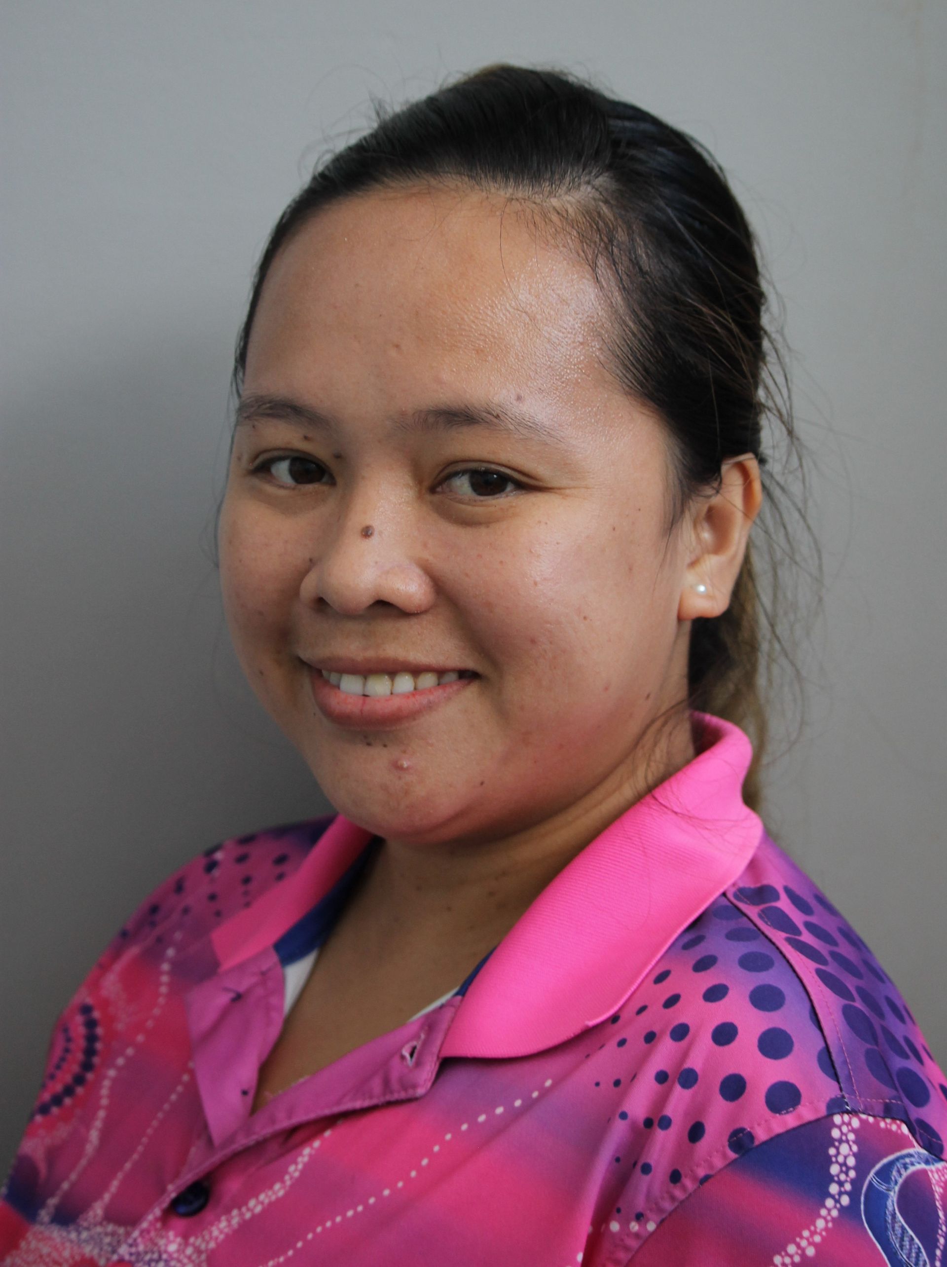Woman with brown hair, wearing pink shirt, smiling at camera.