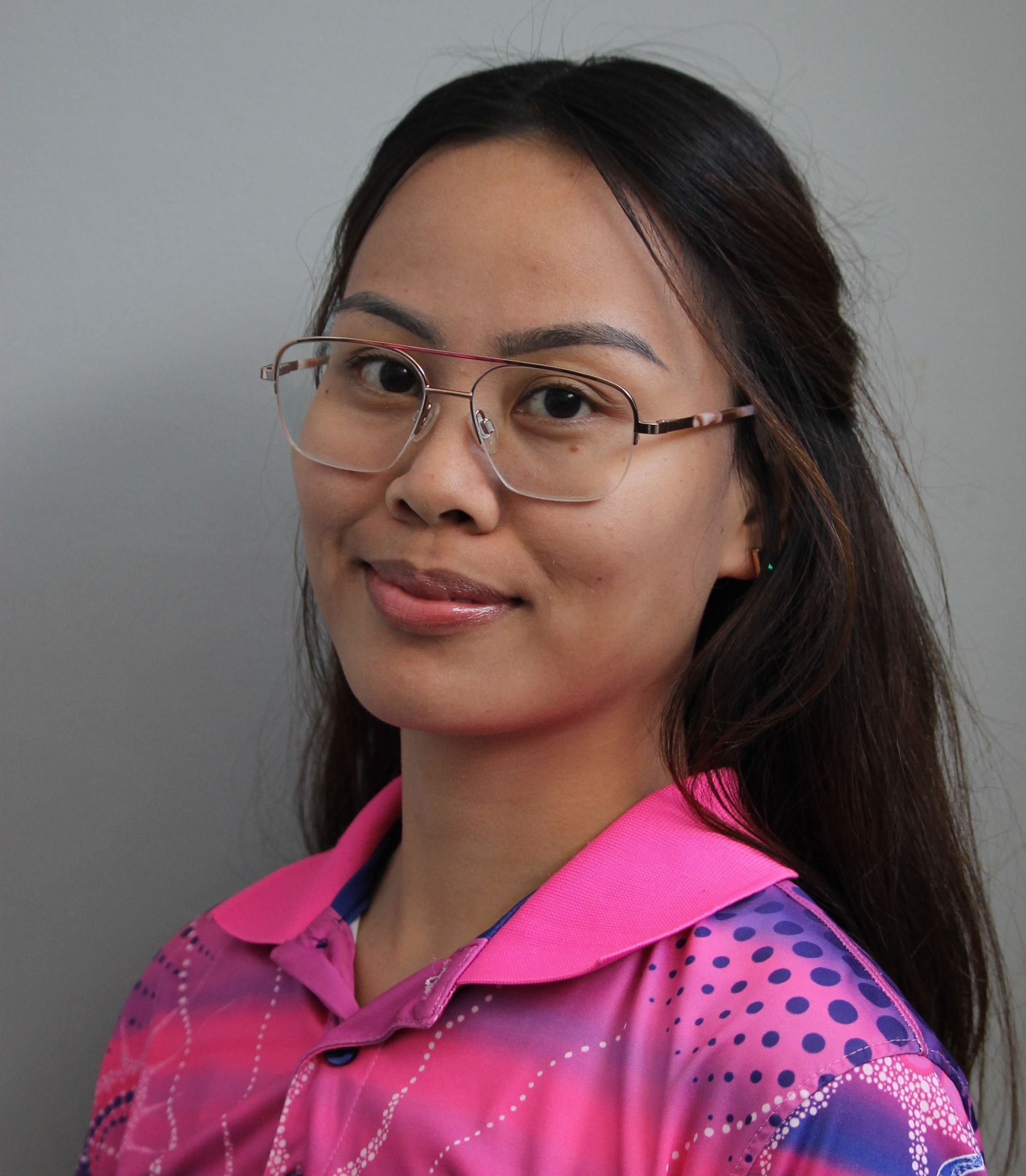 Woman with glasses, brown hair, and pink shirt smiles in front of a gray background.