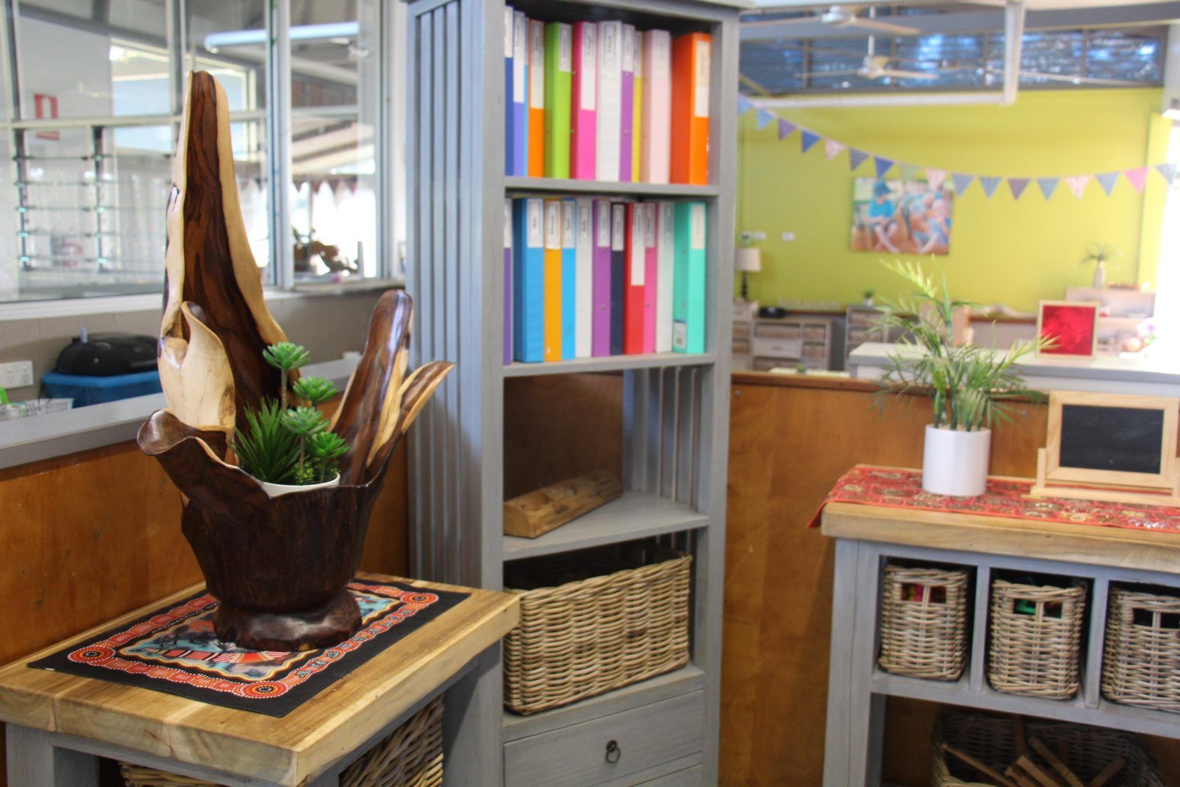An office corner with a wooden shelf full of colorful binders and decorative items.