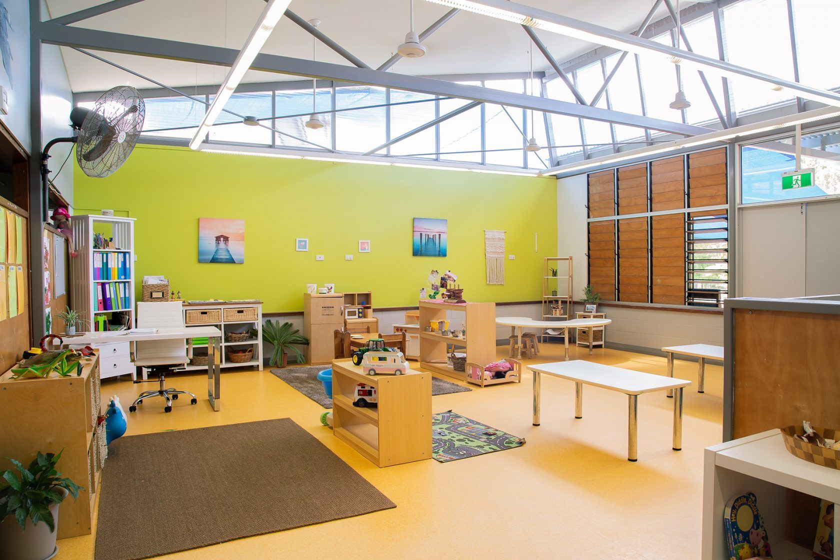 Bright Montessori classroom, lime green wall, wooden tables, open space, natural light.