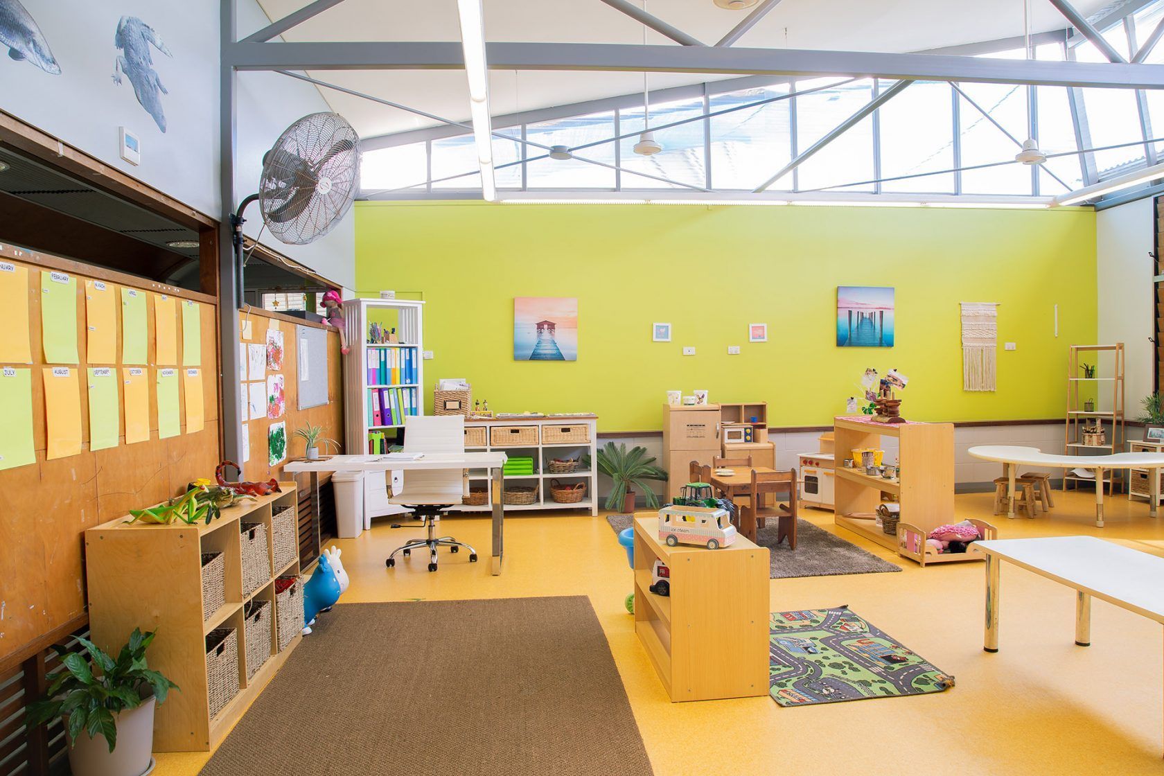 Childcare classroom with yellow walls, play areas, and light-filled windows.