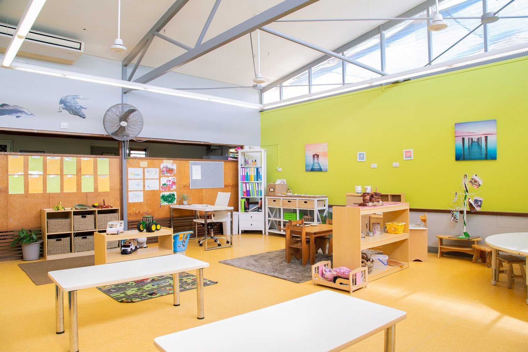 Interior of a brightly colored preschool classroom with tables, toys, and art supplies.
