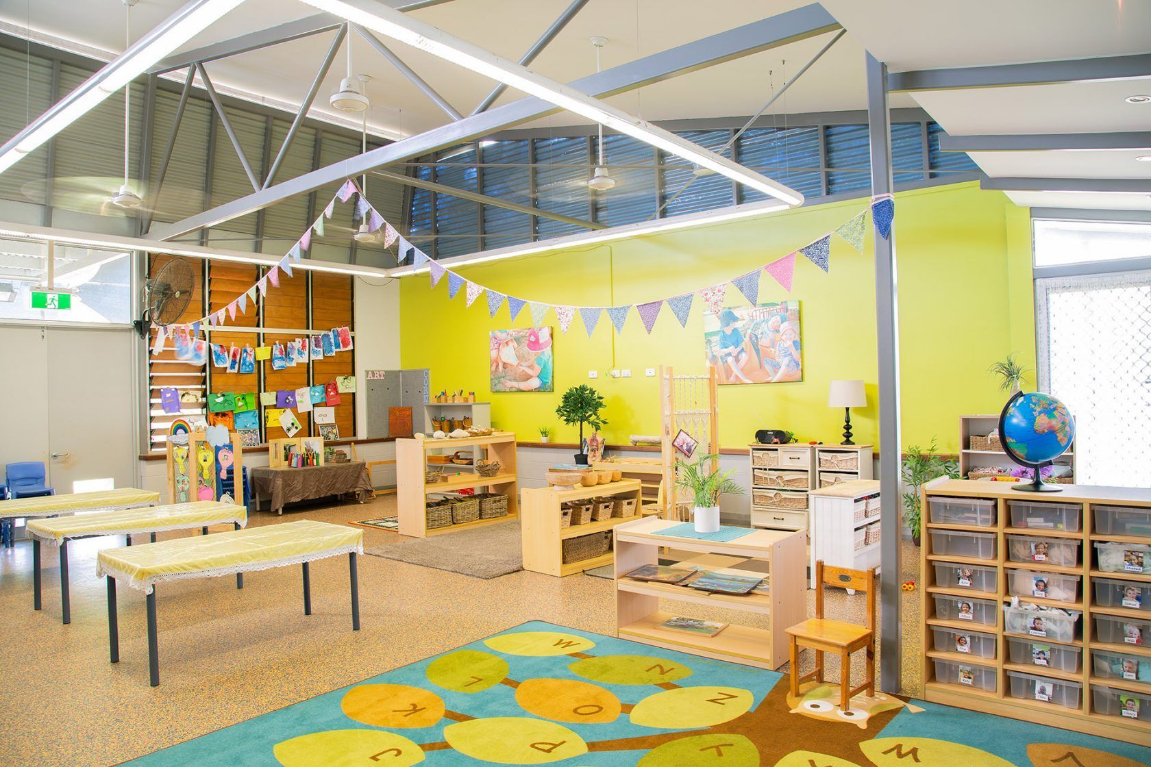 Childcare classroom with tables, colorful rug, and Montessori materials.