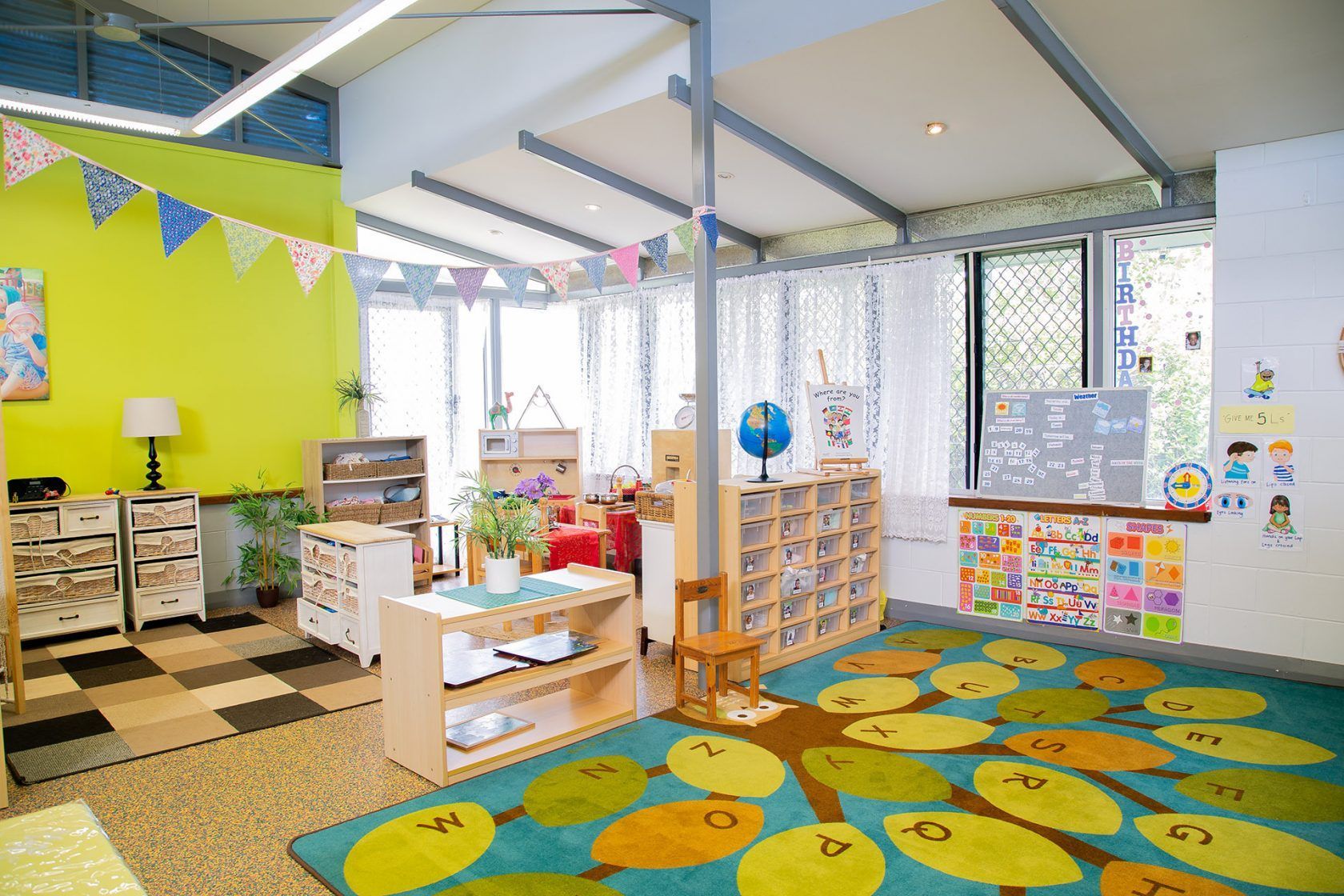 Childcare classroom with colorful decor, books, and tree-shaped rug.