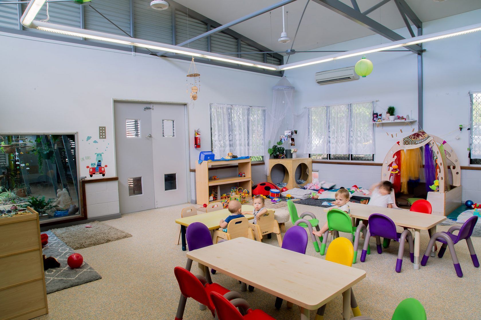 Daycare classroom with kids at tables, toys, and play areas.