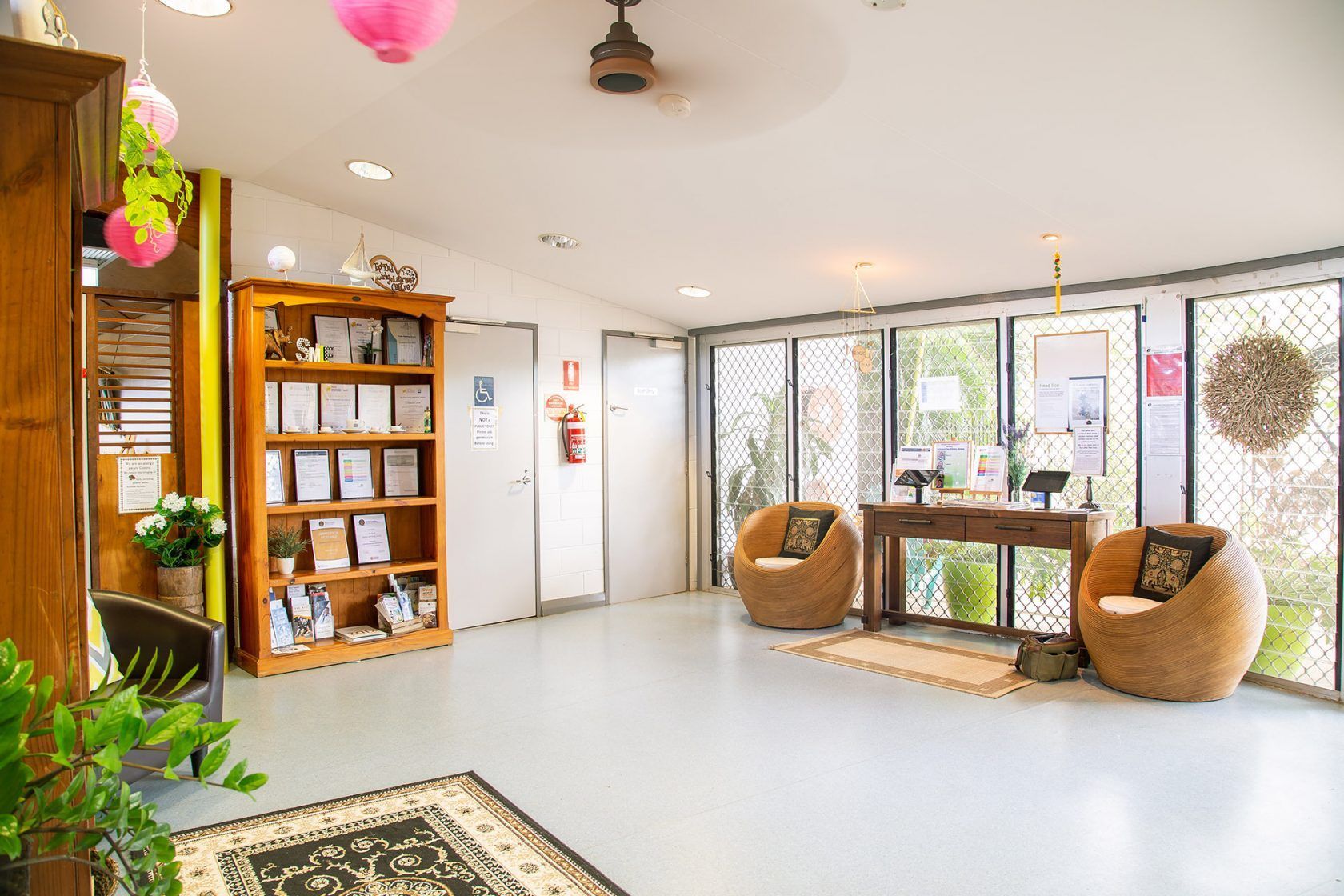 Bright lobby with wooden furniture, seating, and a bookshelf. Pink decorations hang from the ceiling.