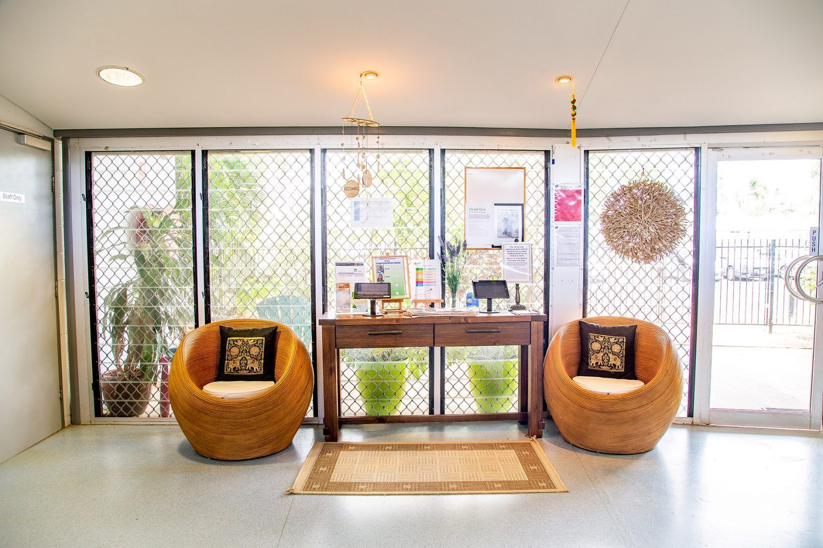 Reception area with wicker chairs, table, rug, plants, and barred windows.
