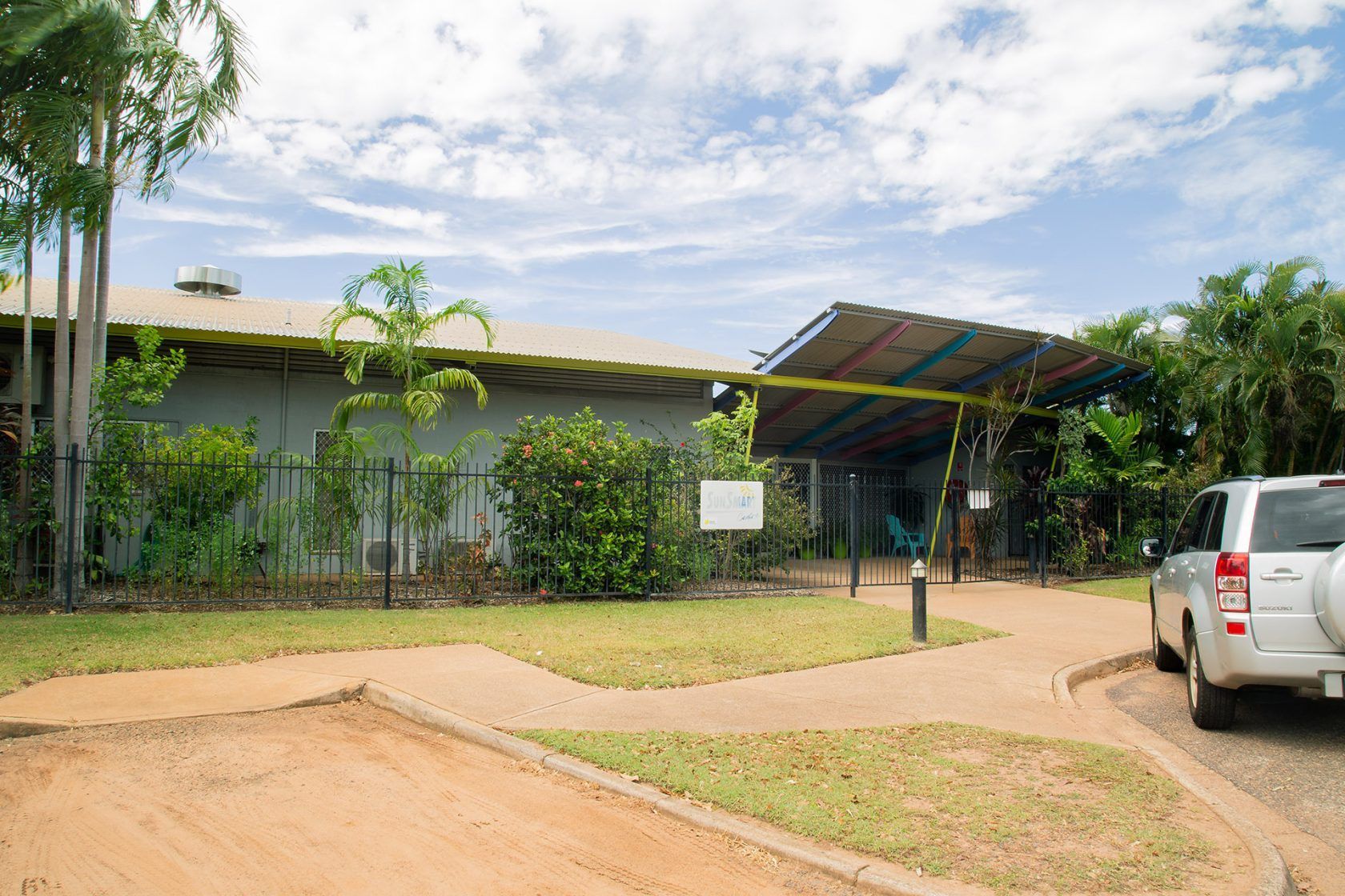 Gray building with a covered entrance, surrounded by green landscaping and a white SUV parked nearby.