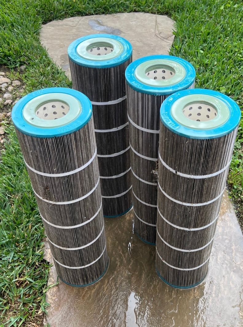 Four filter cartridges are stacked on top of each other on a sidewalk.