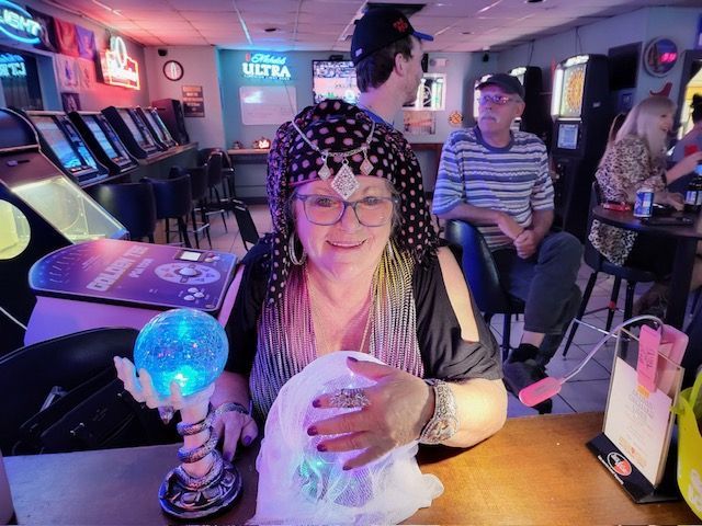 A woman is sitting at a table in an arcade holding a crystal ball.