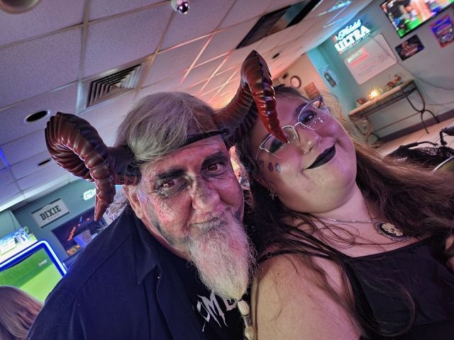 A man and a woman are posing for a picture in a room . the man has horns on his head.