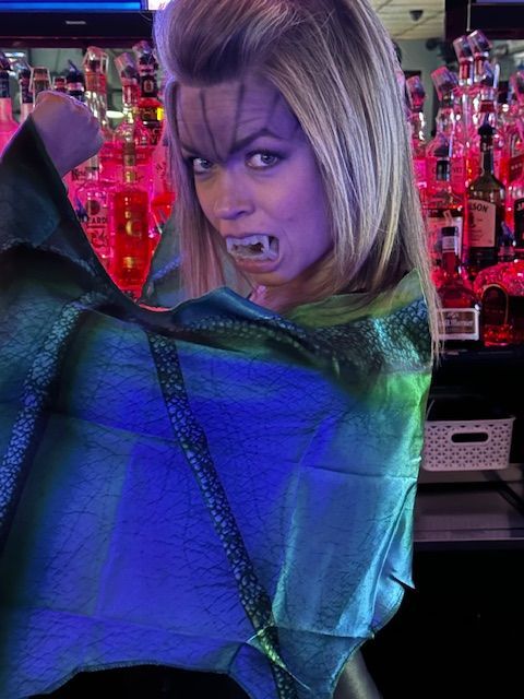 A woman in a bat costume is standing in front of a bar.