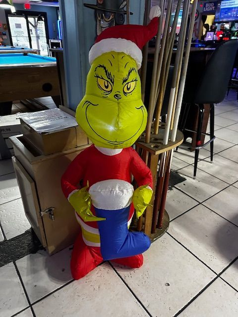 An inflatable grinch holding a christmas stocking in a pool hall