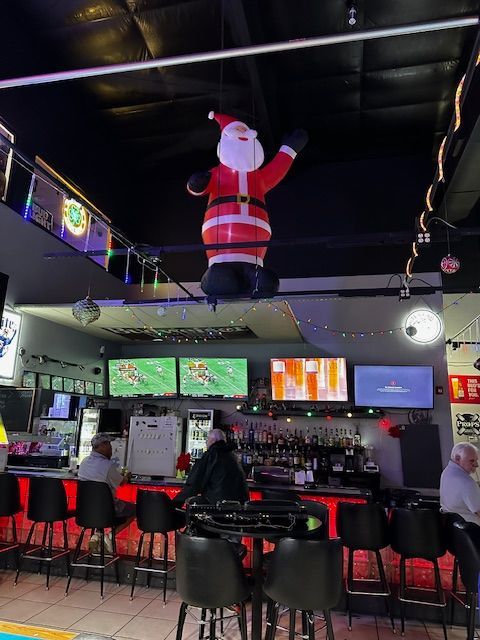 An inflatable santa claus is hanging from the ceiling of a bar