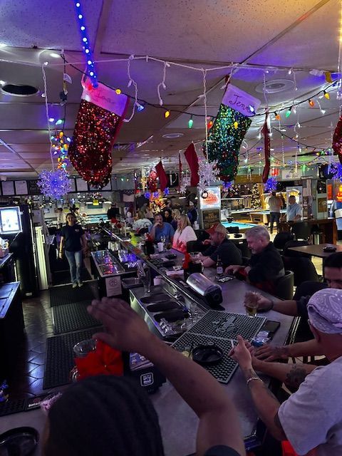 A group of people are sitting at a bar with christmas lights hanging from the ceiling.