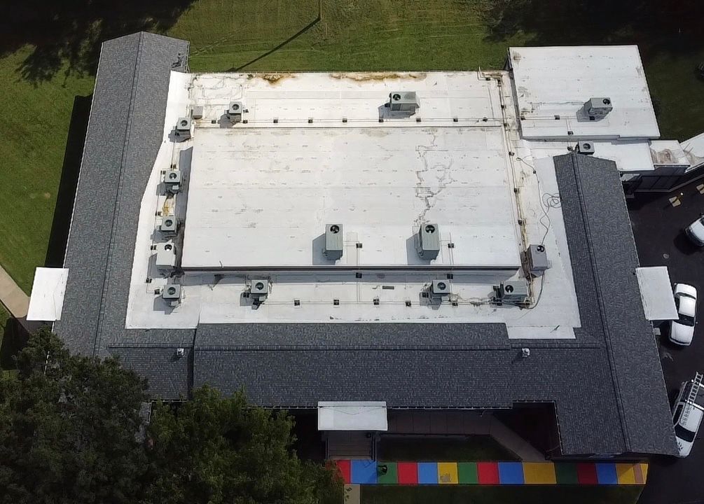 Aerial view of a school building with a flat roof, air conditioning units, and a dark gray shingled perimeter.
