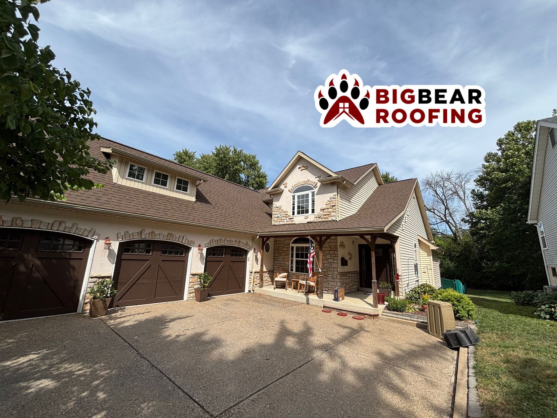 A house with brown roofing, beige walls, and brown garage doors. BigBear Roofing logo on the upper right.
