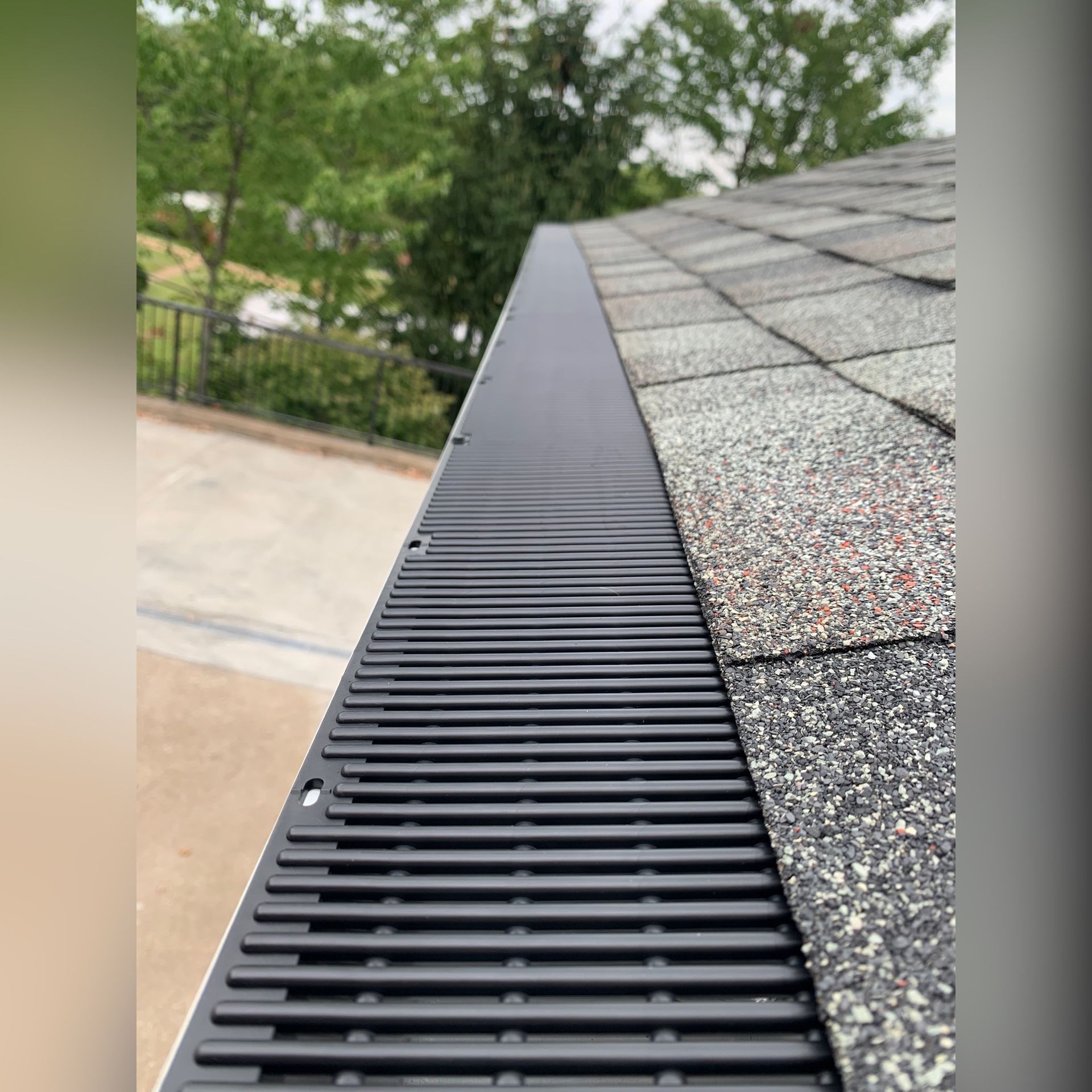 Black gutter guard installed along the edge of a roof with gray and brown shingles.