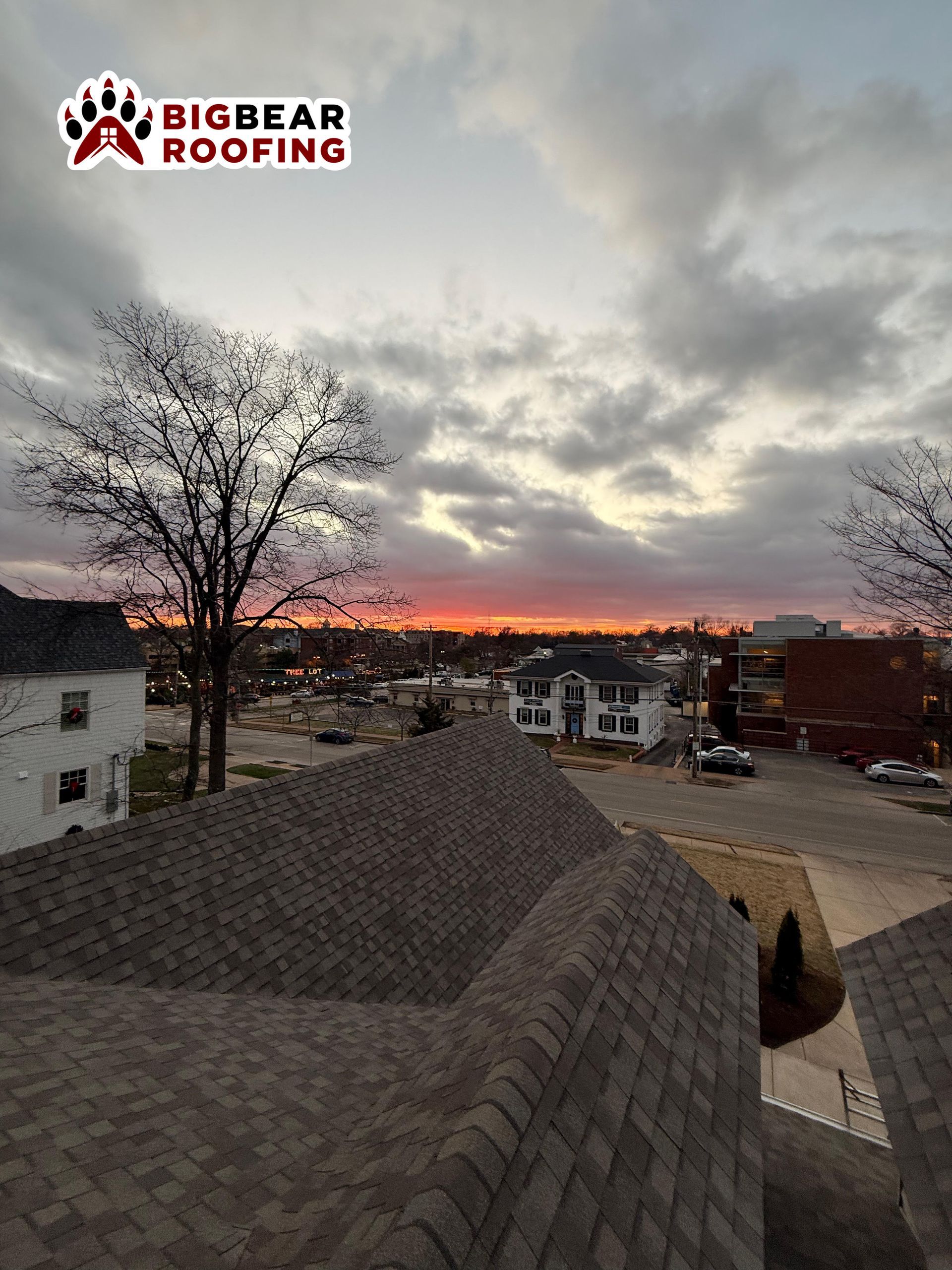 Rooftop view of a town at sunset with the Big Bear Roofing logo in the upper left corner.