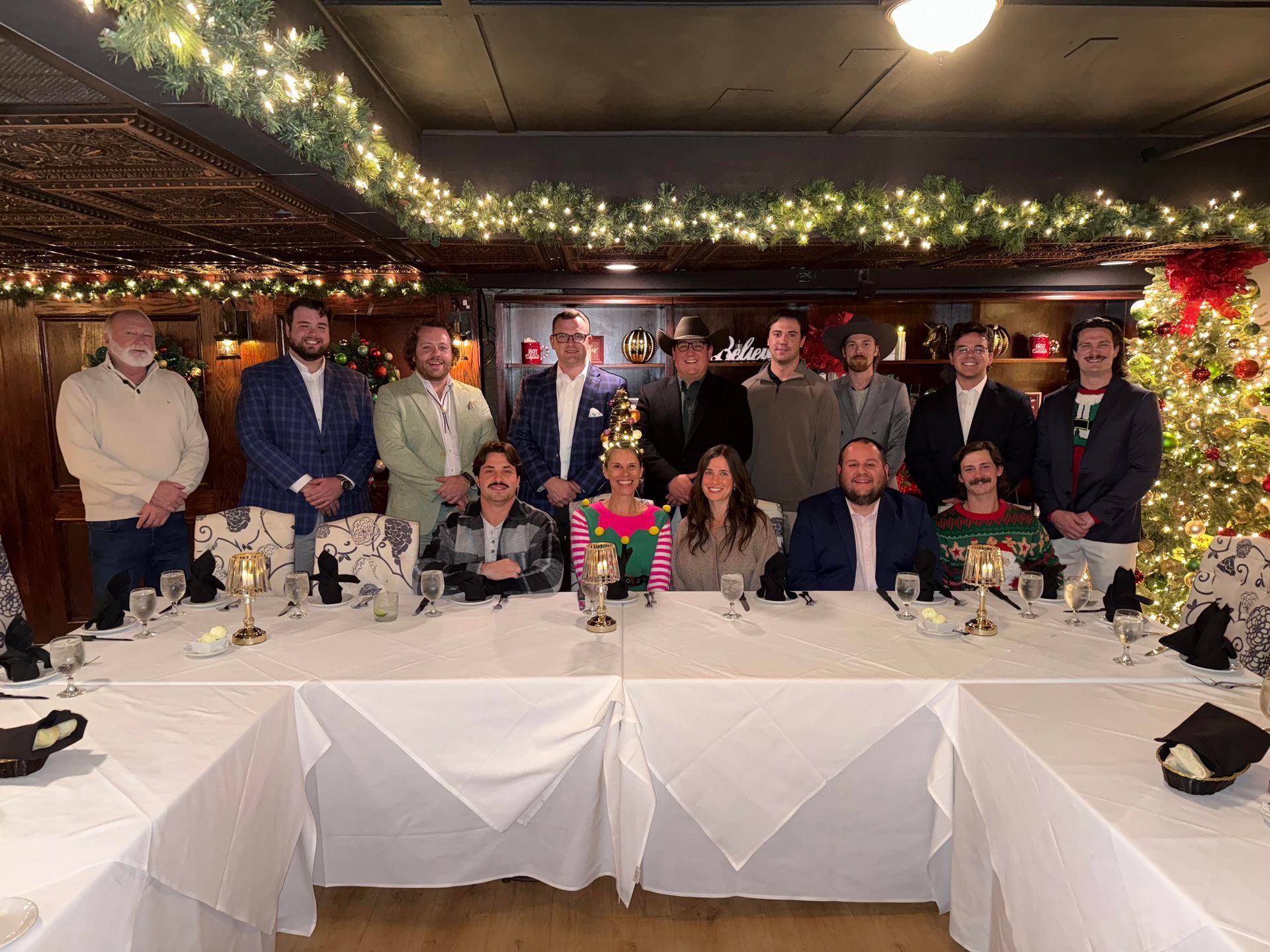 Group of people at a dinner table, decorated for the holidays with lights and a Christmas tree.