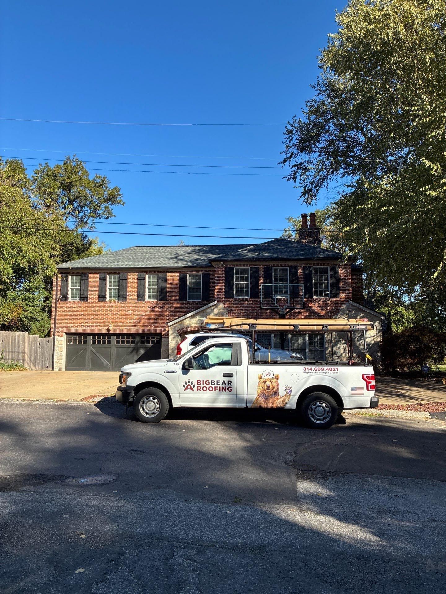 White work truck parked in front of a two-story brick house on a sunny day.